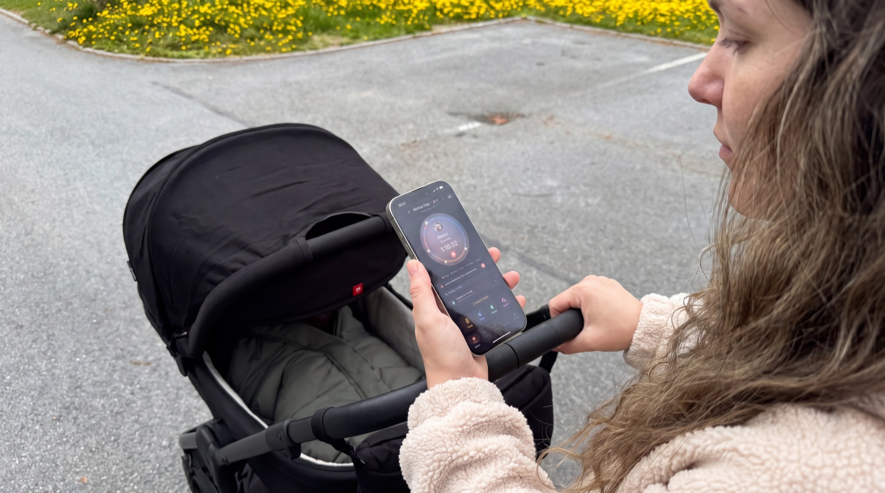 A parent pushing a pram, checking the TandemBaby Orbit on her phone.
